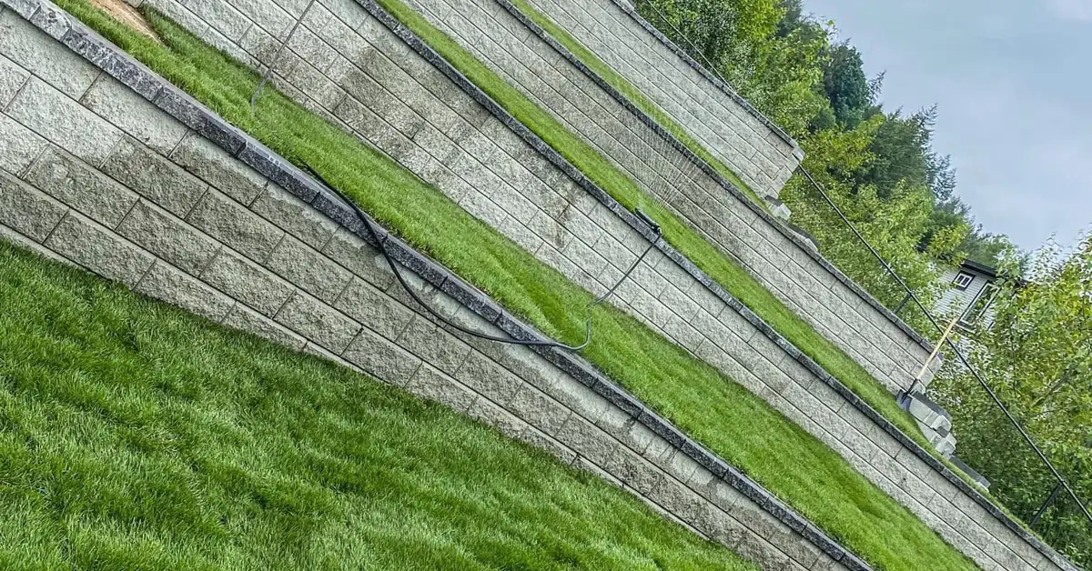 Terraced concrete block retaining walls with lawn on a sloped lot, built to manage backyard drainage in Chilliwack