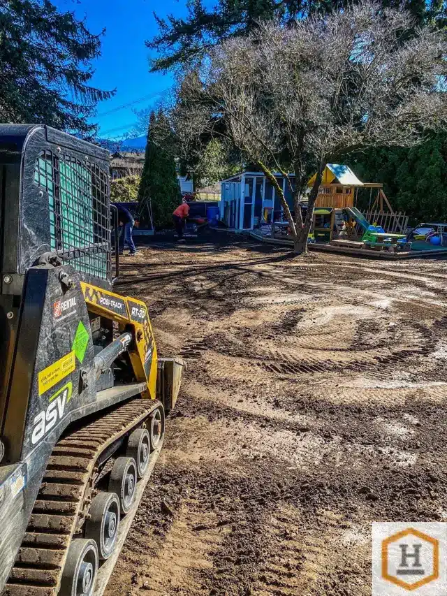 Compact track loader regrading a bare backyard so water drains away from the house