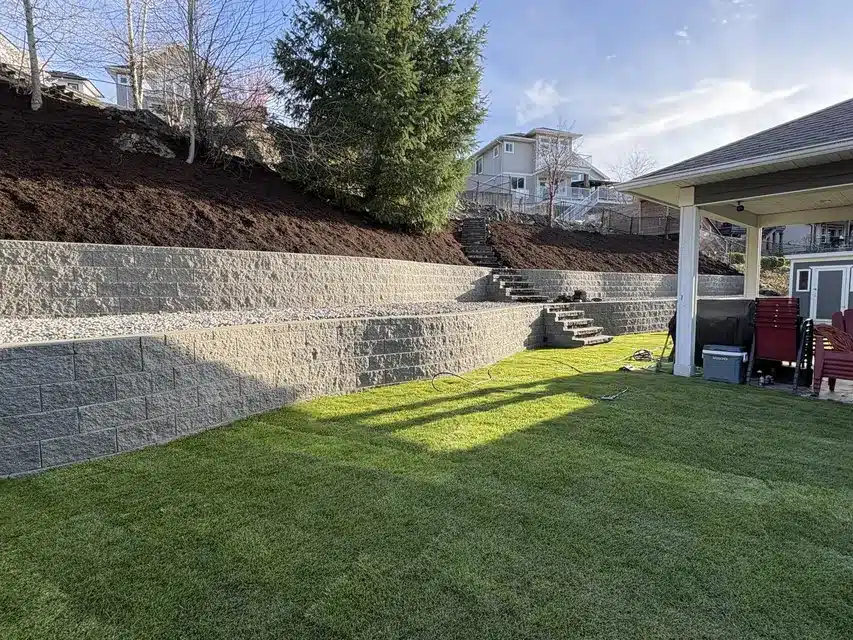 Segmental block retaining wall terracing a slope above new lawn, where catch basin vs french drain choices affect runoff